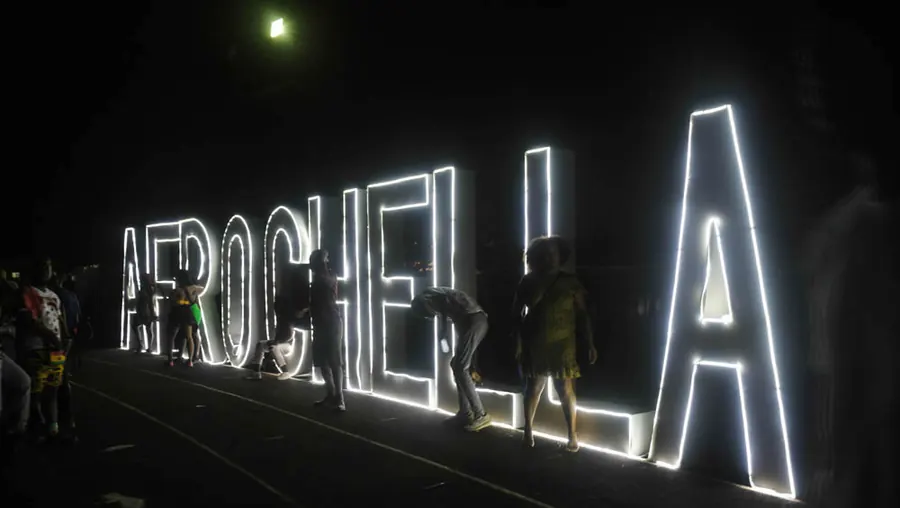 Giant lit-up letters spelling Afrochella at night, with people taking photos