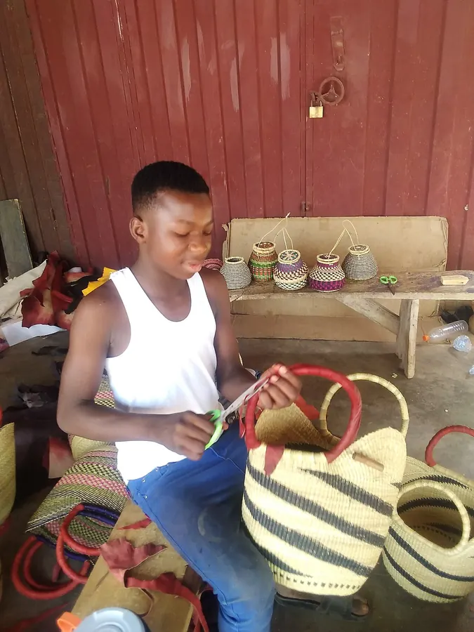 A boy in Bolgatanga weaving a striped basket