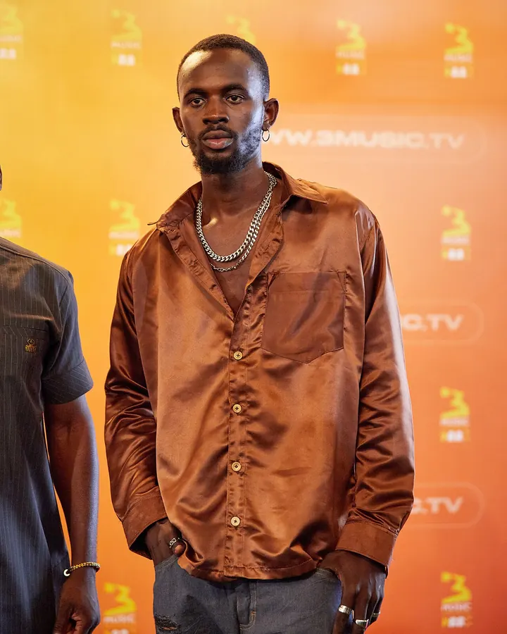 Black Sherif holding an award in front of a pink wall