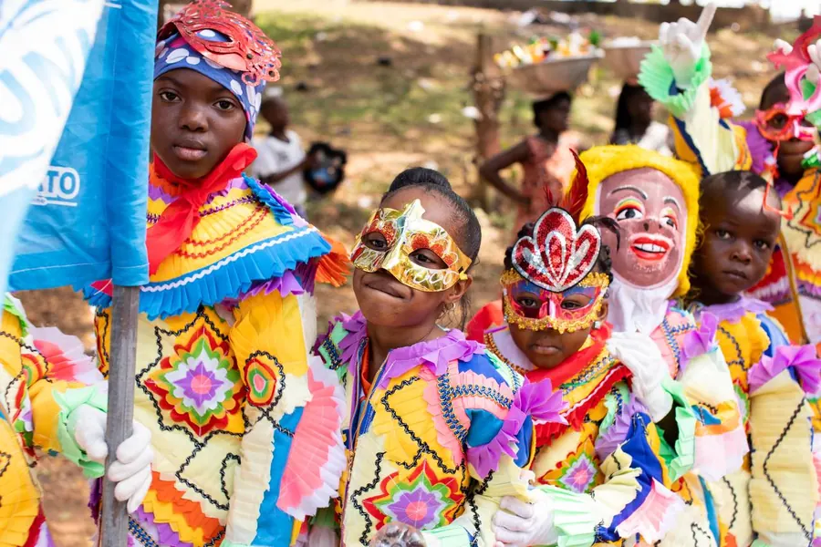 Masqueraders in painted masks and patterned costumes holding flags