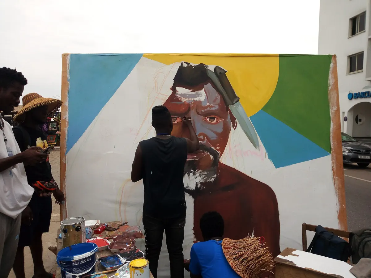 An artist paints a large portrait mural at Chale Wote