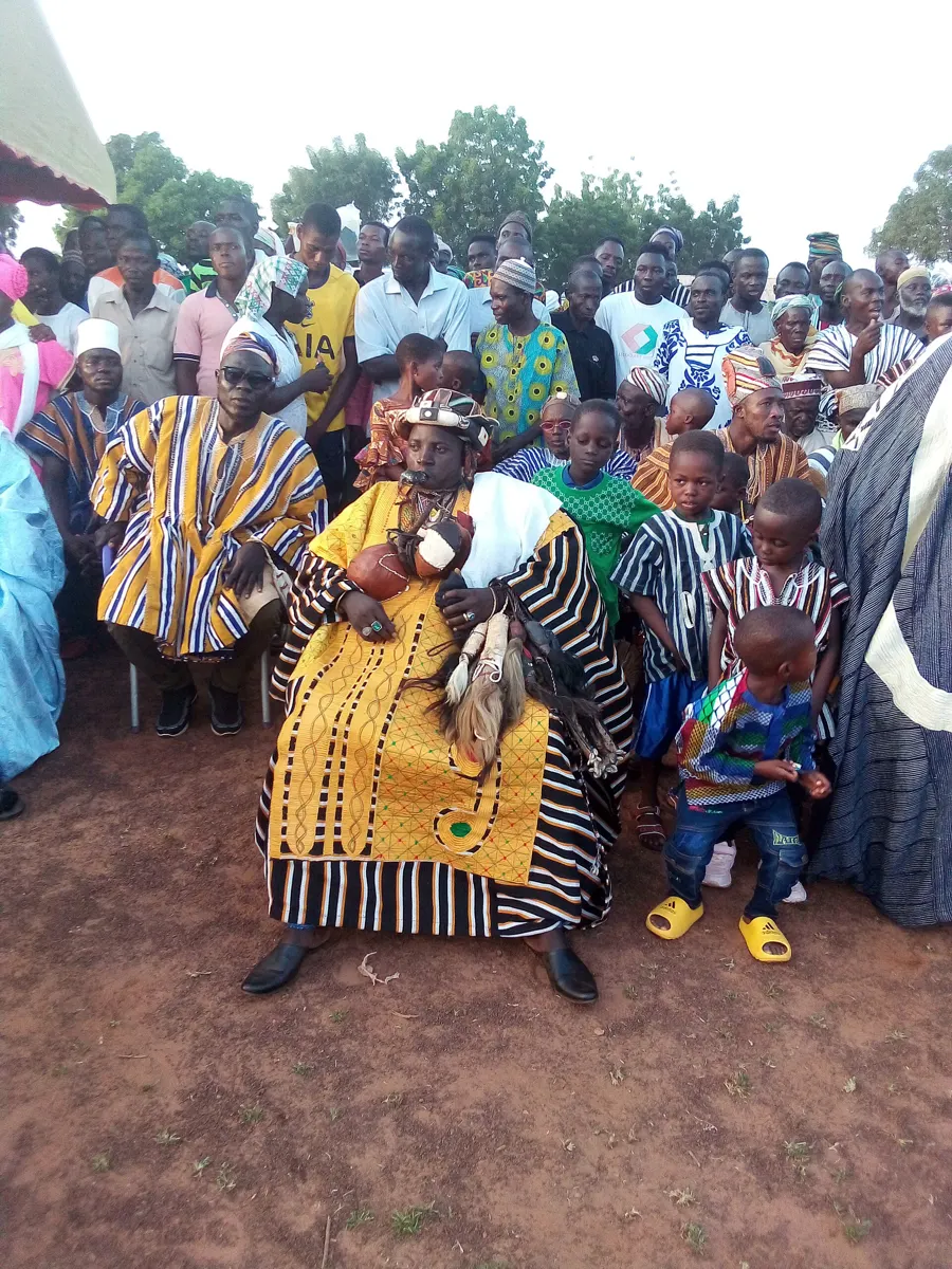 A seated elder in yellow surrounded by a crowd at Damba