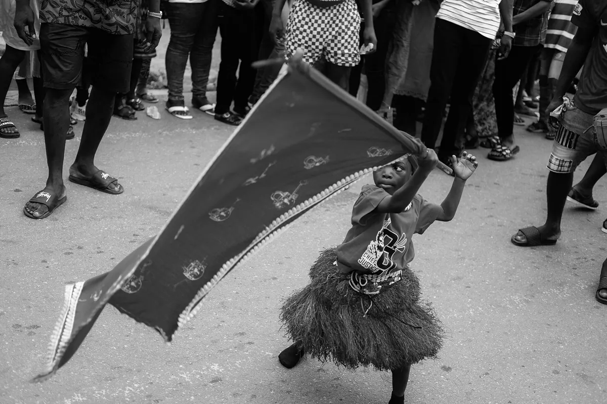A girl in a raffia skirt waves an Asafo company flag in the street