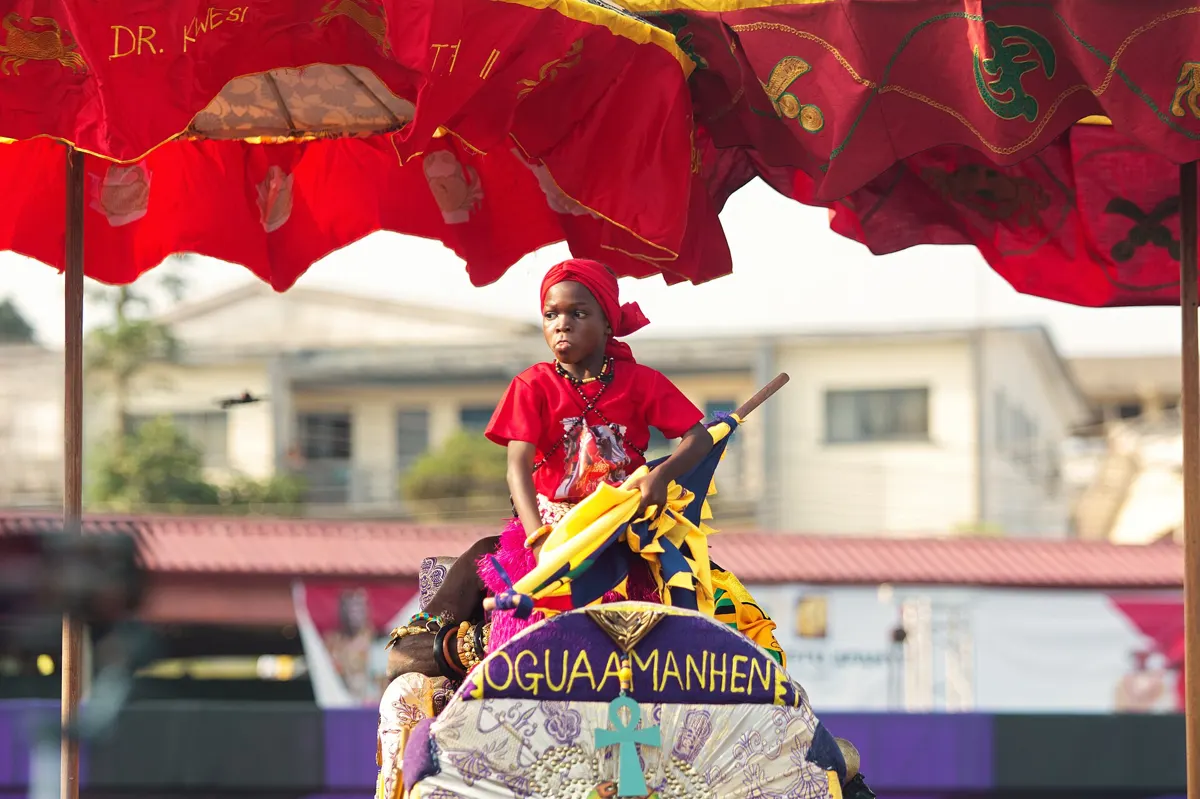 A young participant carried under a red umbrella in the Fetu Afahye procession